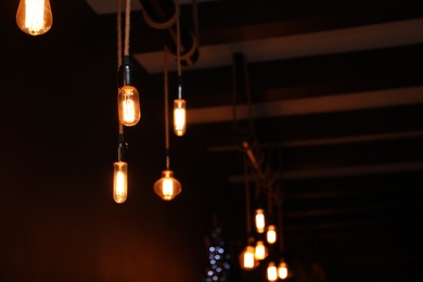 Photo of Glowing lamp bulbs in dark room. Space for text