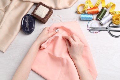 Woman with sewing needle and thread embroidering on cloth at white wooden table, top view