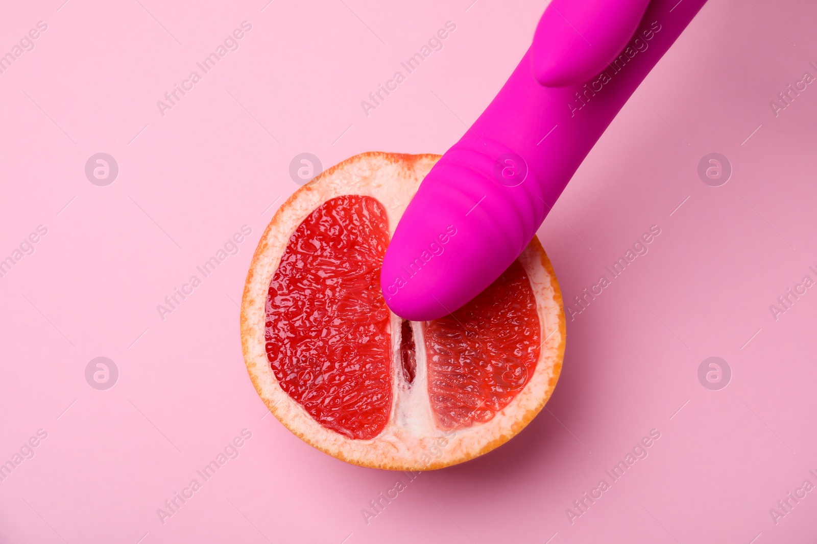 Photo of Half of grapefruit and purple vibrator on pink background, flat lay. Sex concept