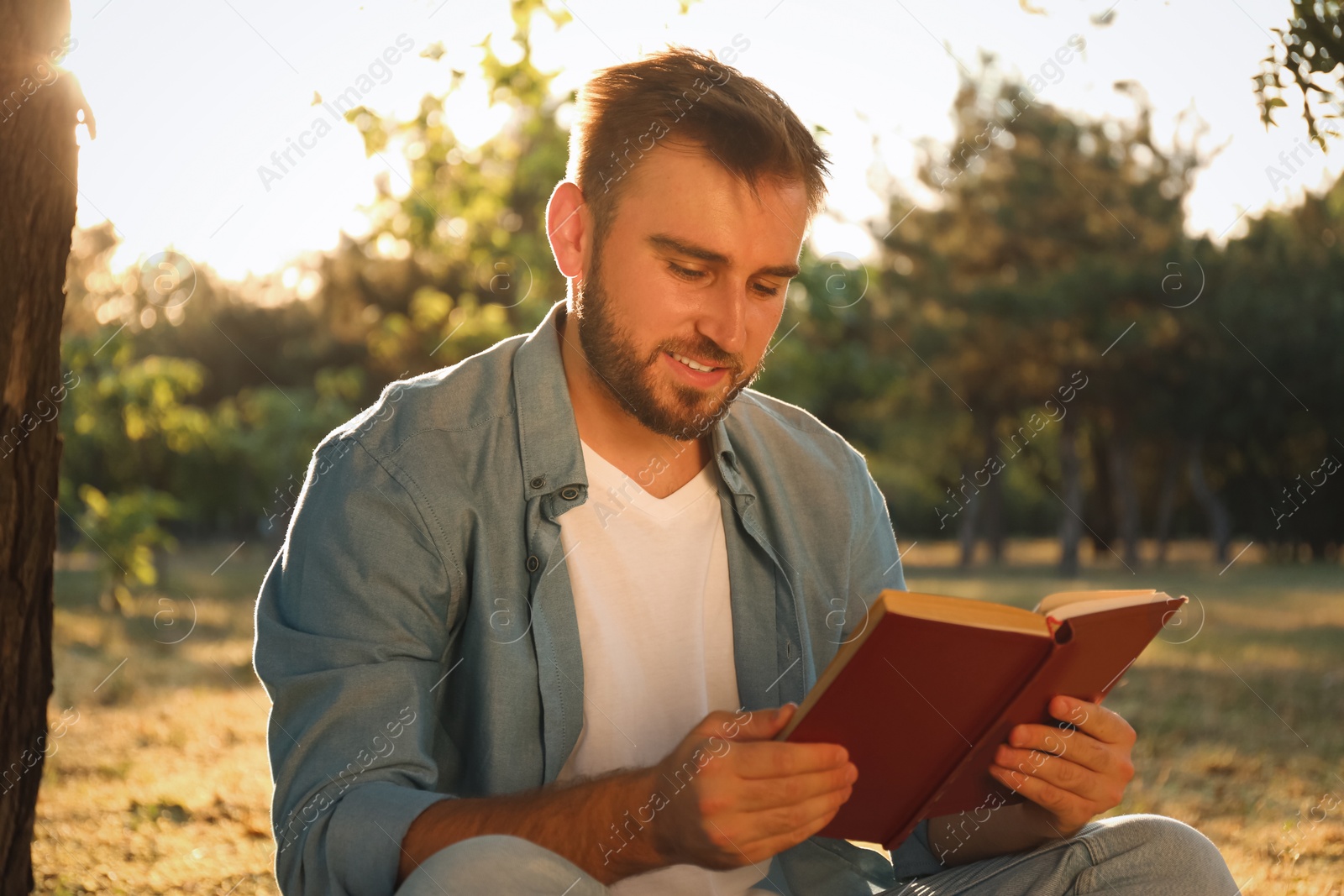 Photo of Young man reading book near tree in park