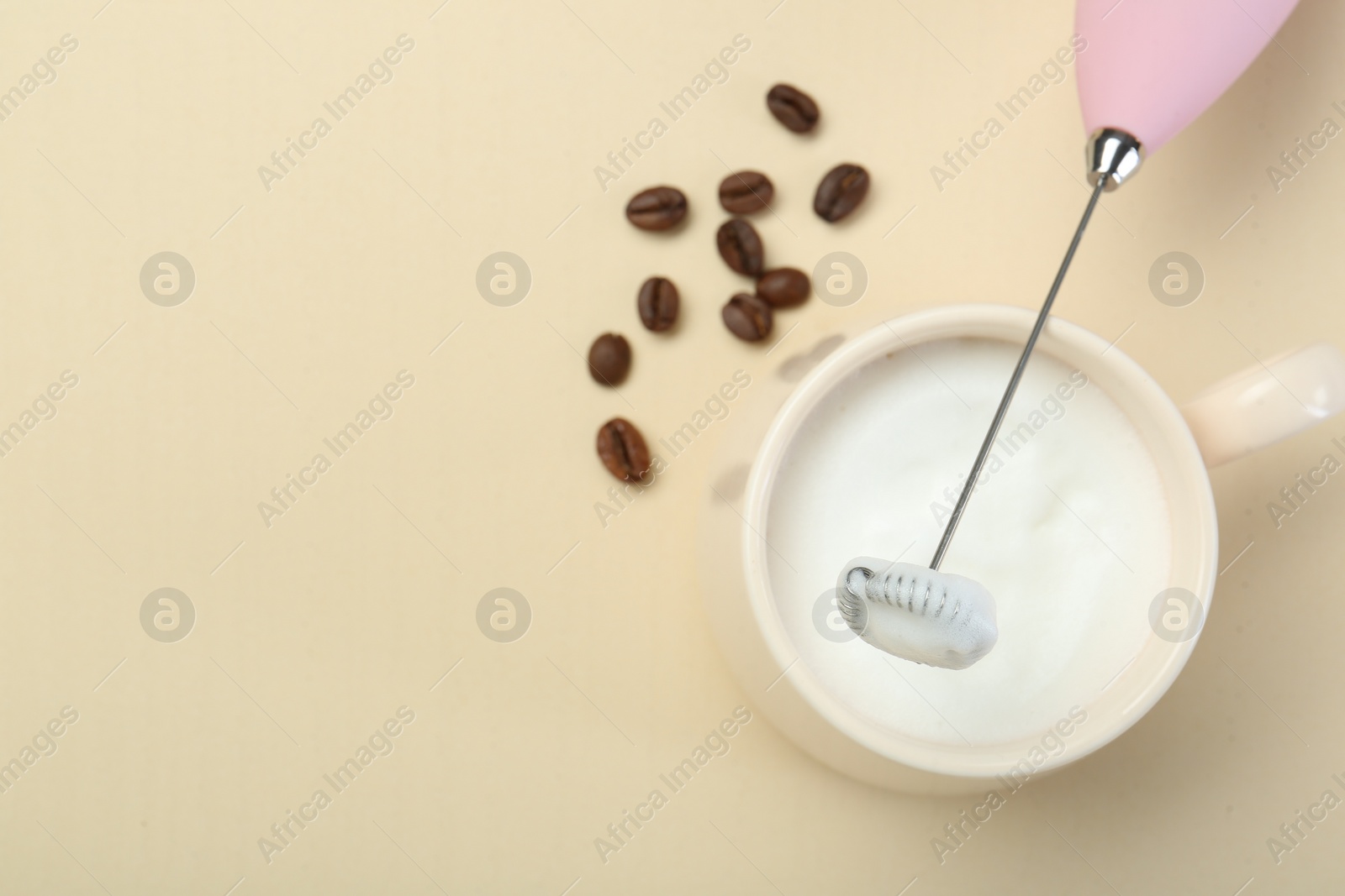 Photo of Mini mixer (milk frother), cup of whipped milk and coffee beans on beige background, flat lay. Space for text