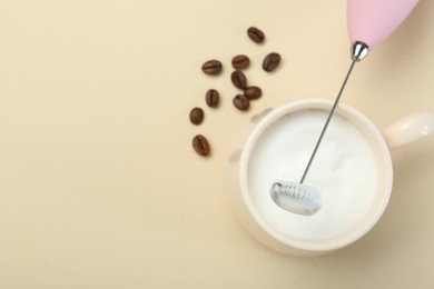 Mini mixer (milk frother), cup of whipped milk and coffee beans on beige background, flat lay. Space for text