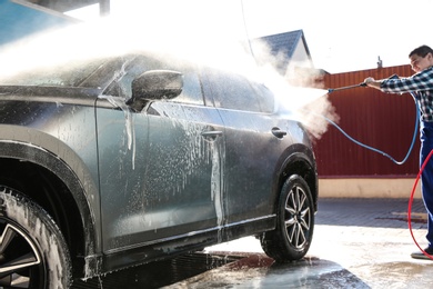 Worker cleaning automobile with high pressure water jet at car wash