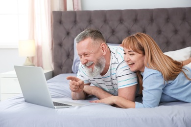 Photo of Mature couple using laptop on bed at home