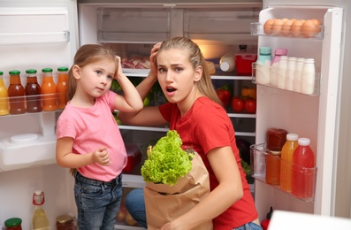 Photo of Emotional young mother and daughter near refrigerator at home
