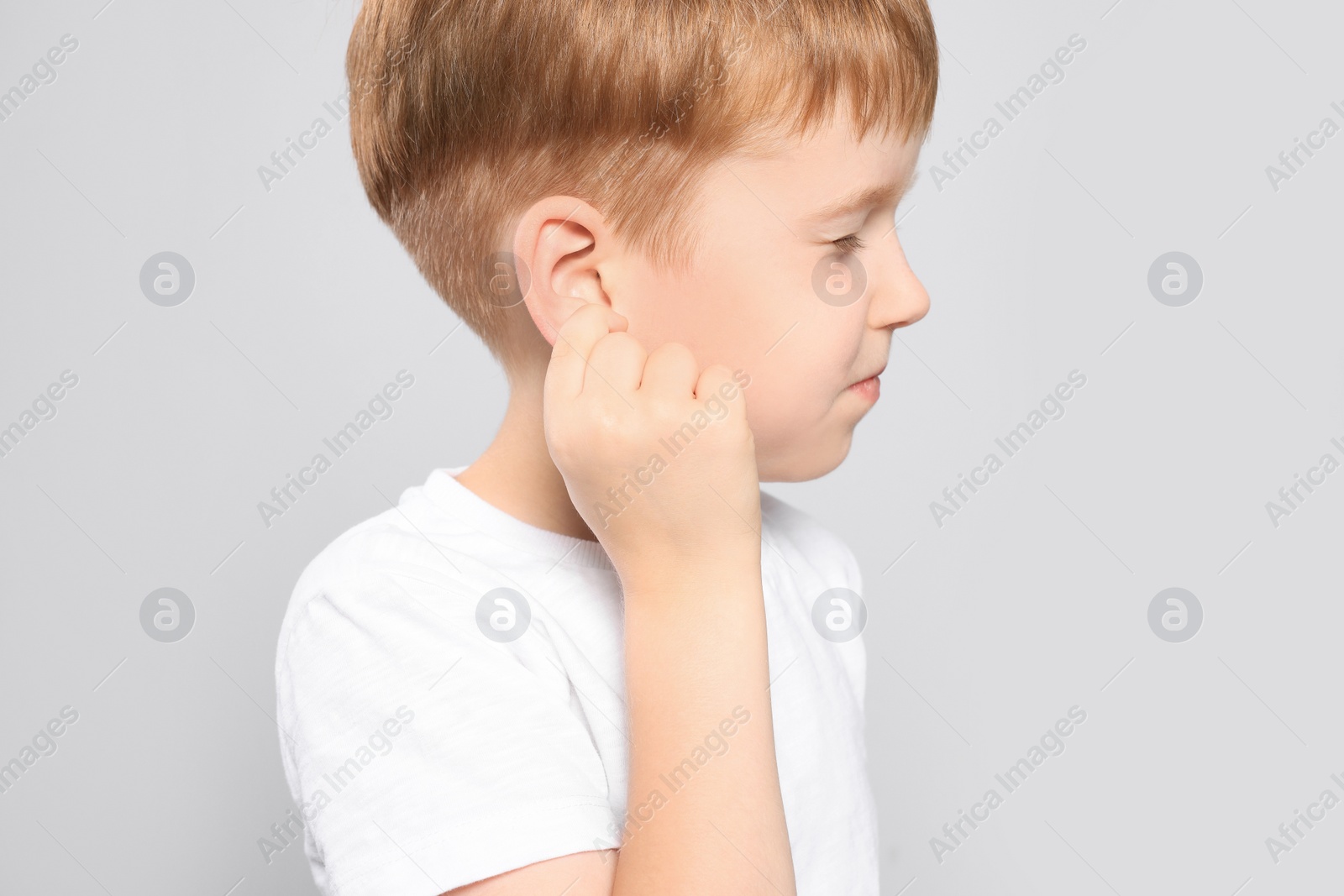 Photo of Little boy suffering from ear pain on light grey background, closeup