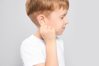 Little boy suffering from ear pain on light grey background, closeup