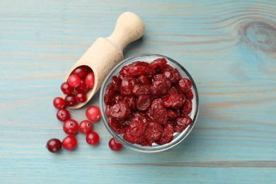 Photo of Tasty dried cranberries in bowl and fresh ones on light blue wooden table, top view