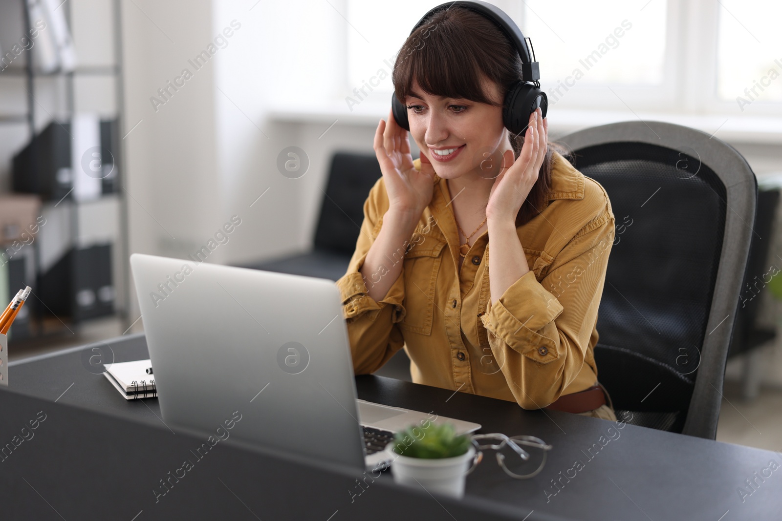 Photo of Woman in headphones watching webinar at table in office