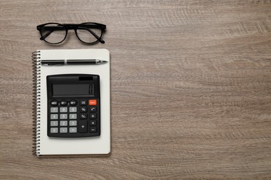 Calculator, office stationery and glasses on wooden table, top view. Space for text