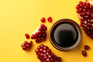 Photo of Glass bowl of tasty pomegranate sauce and fresh ripe fruit on yellow background, flat lay. Space for text
