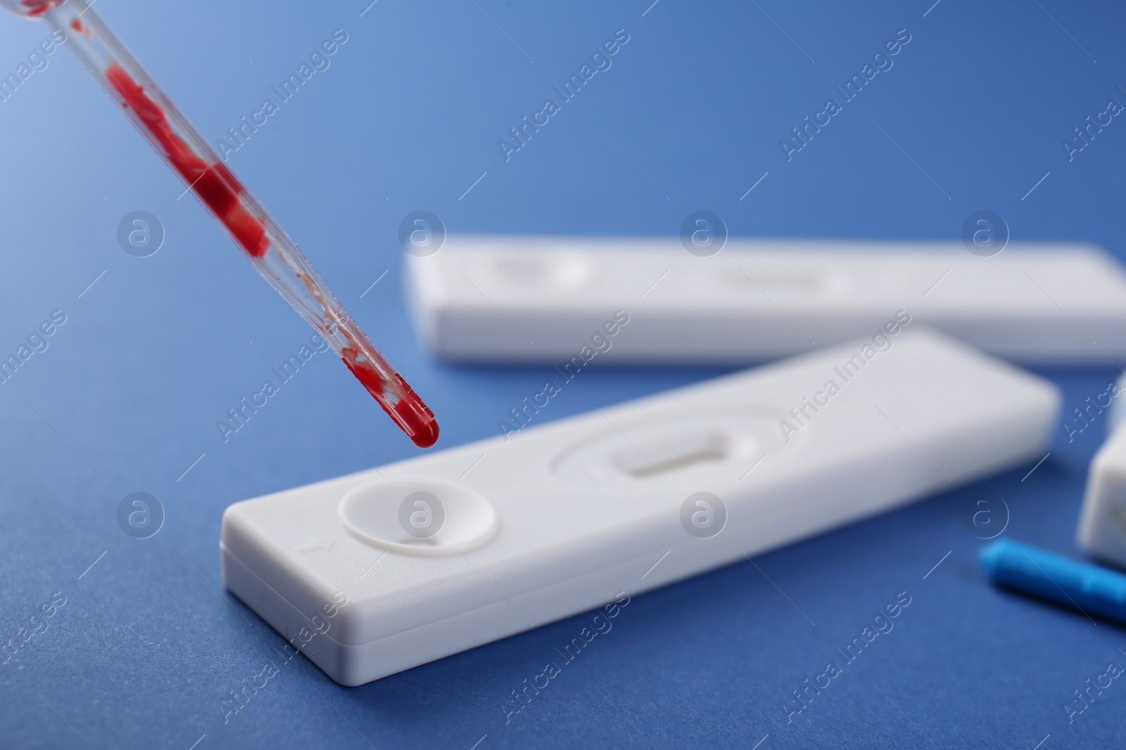 Photo of Dropping blood sample onto disposable express test cassette with pipette on blue background, closeup