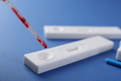 Photo of Dropping blood sample onto disposable express test cassette with pipette on blue background, closeup