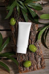 Photo of Tube of cream, olives and leaves on wooden table, flat lay