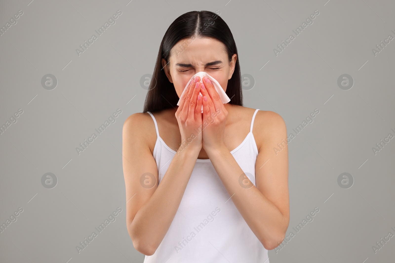 Photo of Suffering from allergy. Young woman blowing her nose in tissue on light grey background