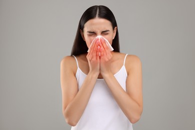 Photo of Suffering from allergy. Young woman blowing her nose in tissue on light grey background