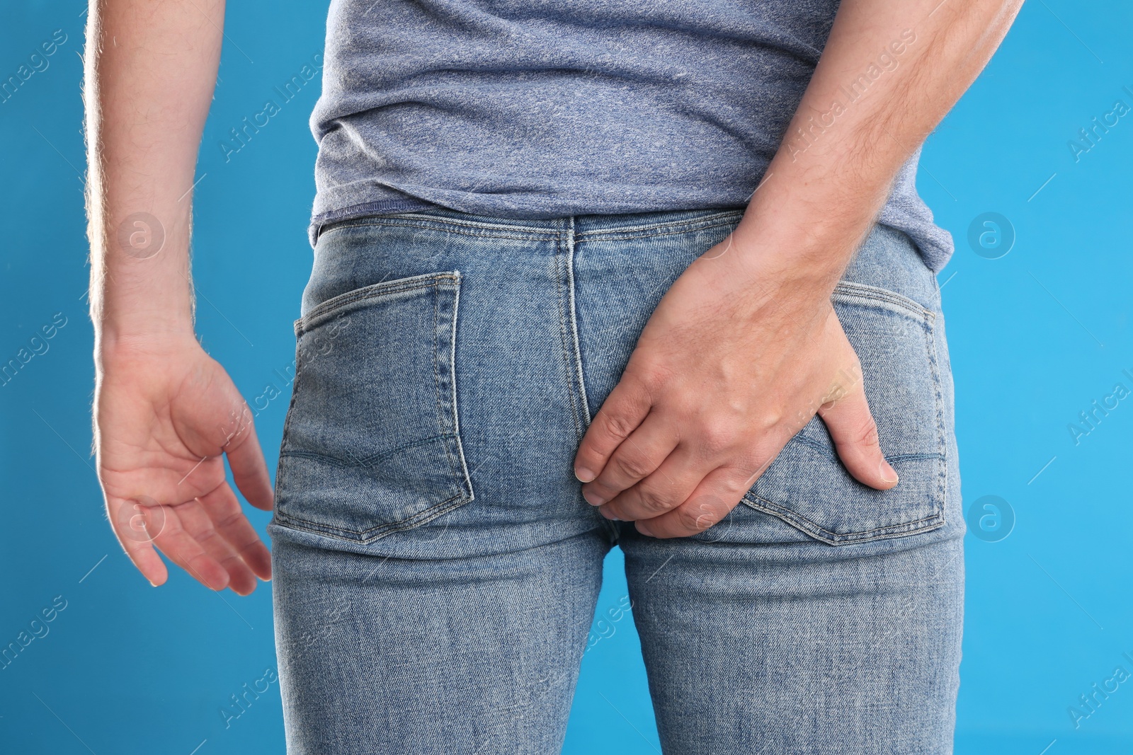 Photo of Man suffering from hemorrhoid on light blue background, closeup