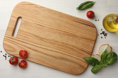 Photo of Cutting board, basil, onion, oil and tomatoes on white wooden table, flat lay. Space for text