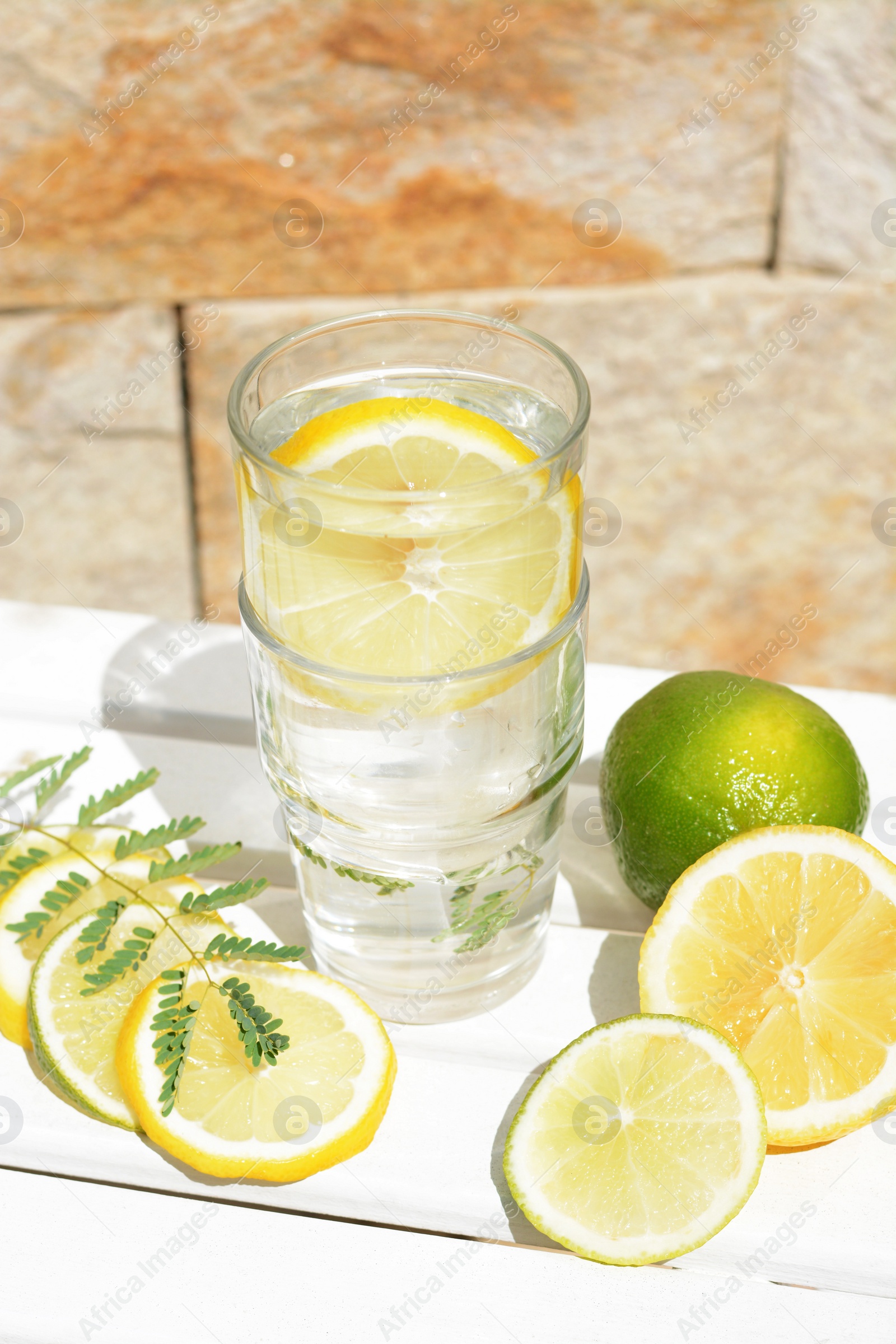 Photo of Delicious refreshing lemonade and pieces of citrus on white wooden table outdoors