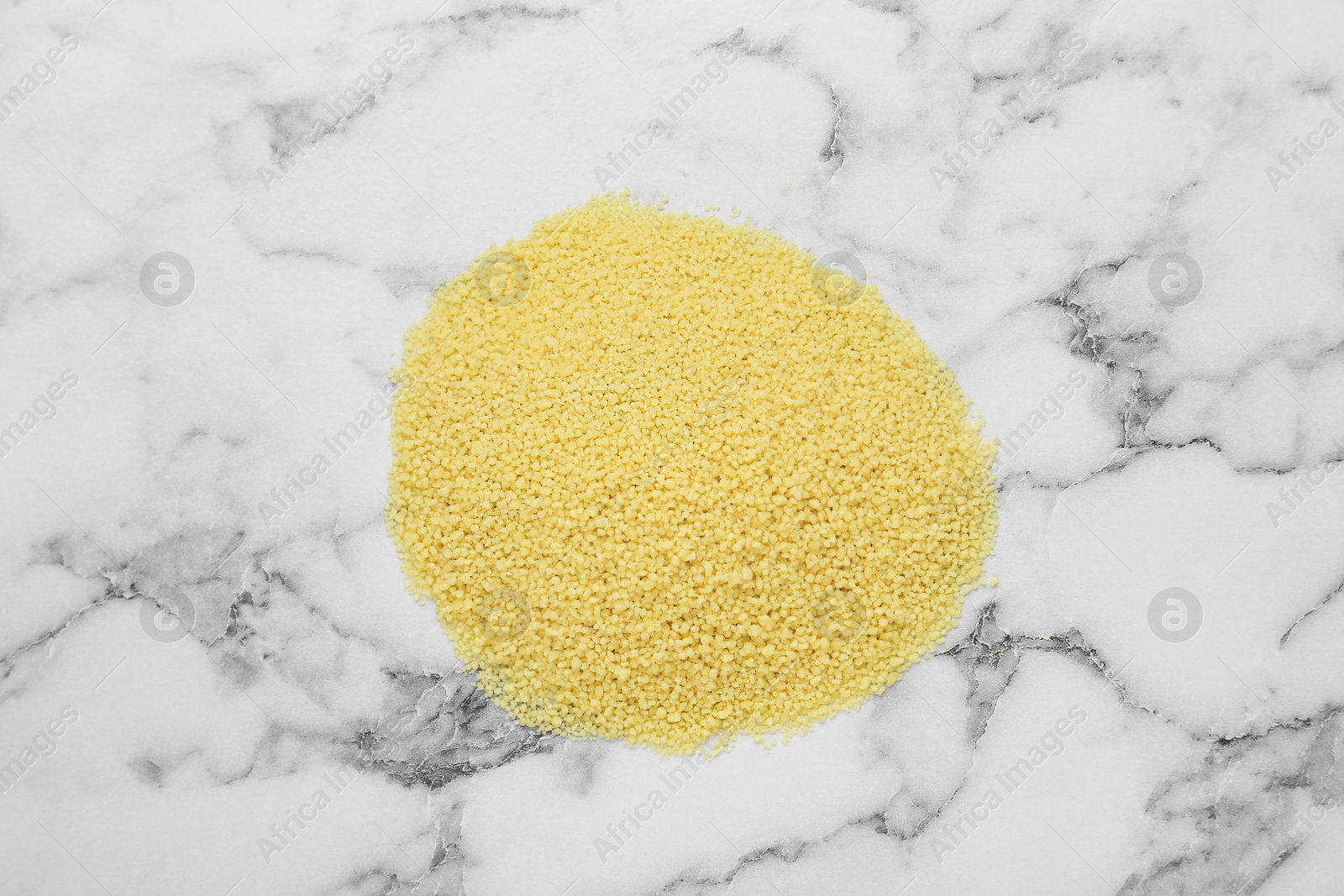 Photo of Heap of raw couscous on white marble table, top view