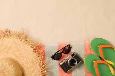 Beach towel, hat, sunglasses, camera and flip flops on sand, flat lay. Space for text