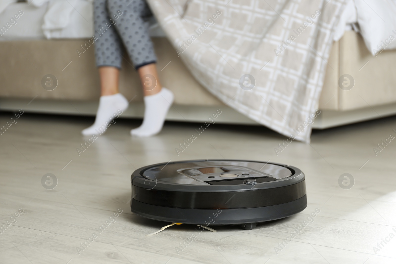 Photo of Modern robotic vacuum cleaner and blurred woman on background