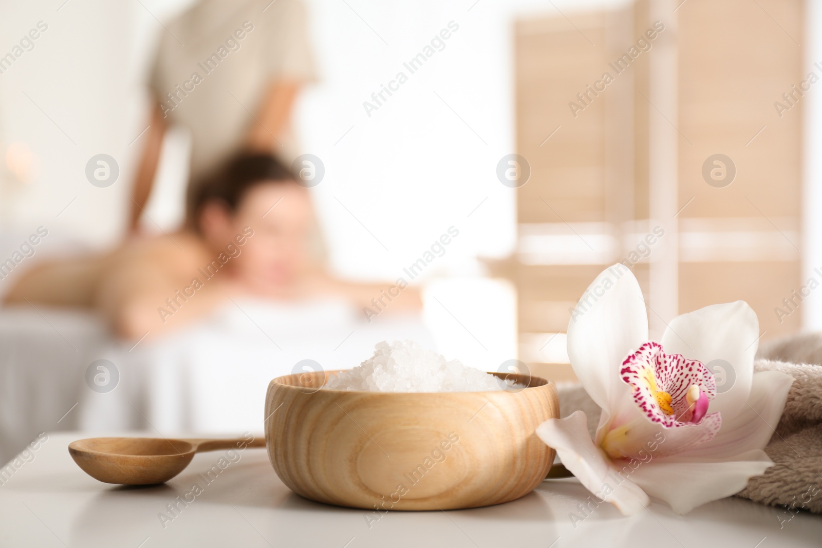 Photo of Bowl with sea salt and orchid flower on white table in spa salon. Space for text