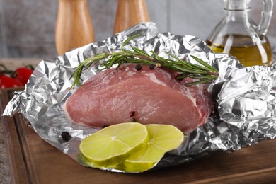 Photo of Aluminum foil with raw meat, rosemary, lime and spices on wooden table, closeup