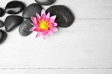 Stones with lotus flower and space for text on white wooden background, flat lay. Zen lifestyle