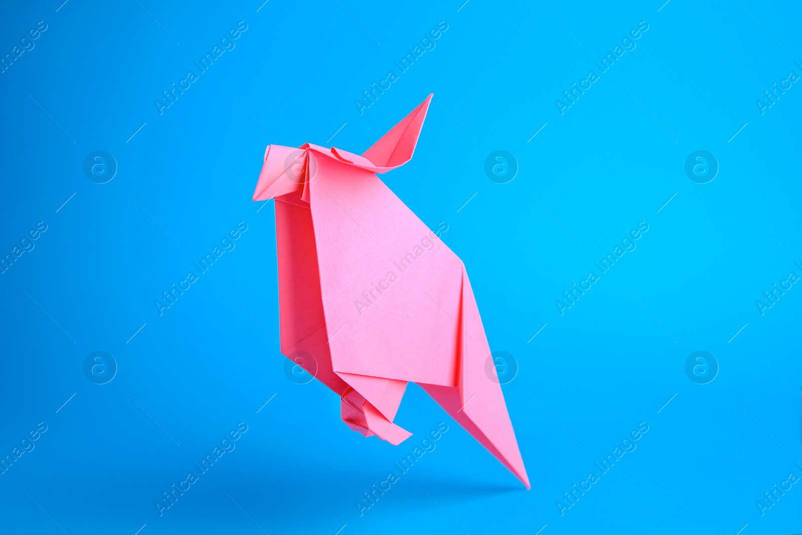 Photo of Origami art. Handmade pink paper parrot on light blue background