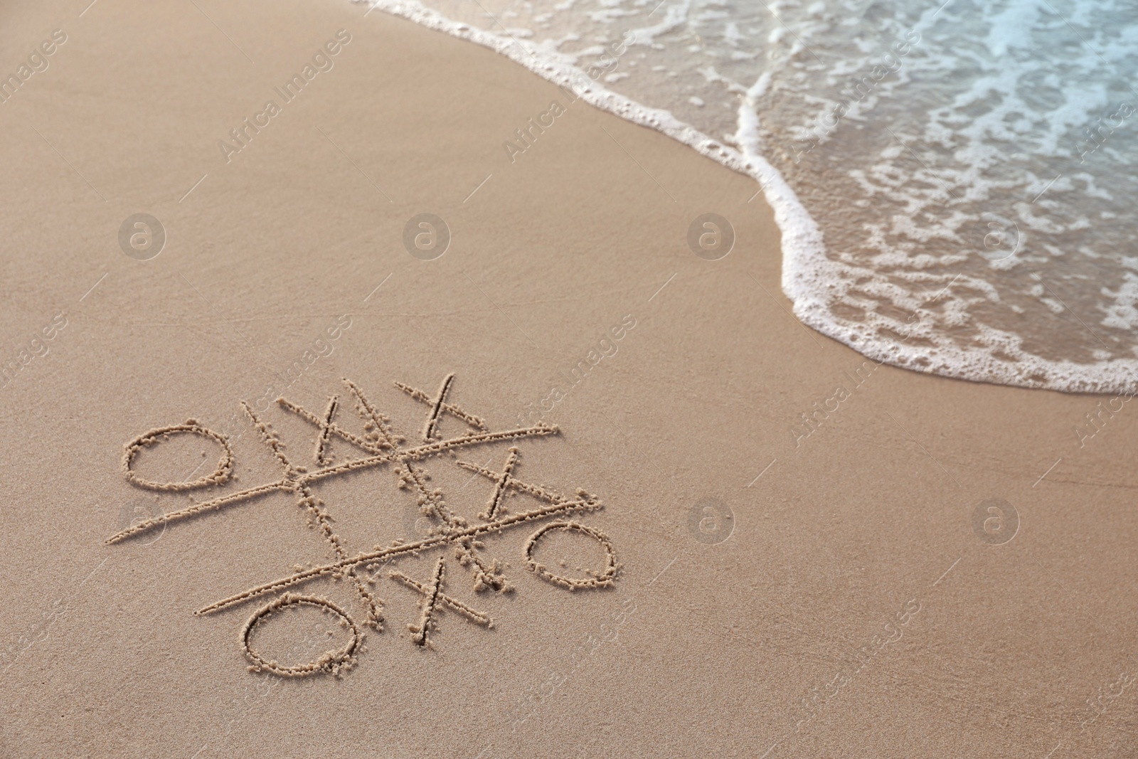 Photo of Tic tac toe game drawn on sand near sea, space for text