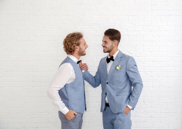 Happy newlywed gay couple in suits against white wall