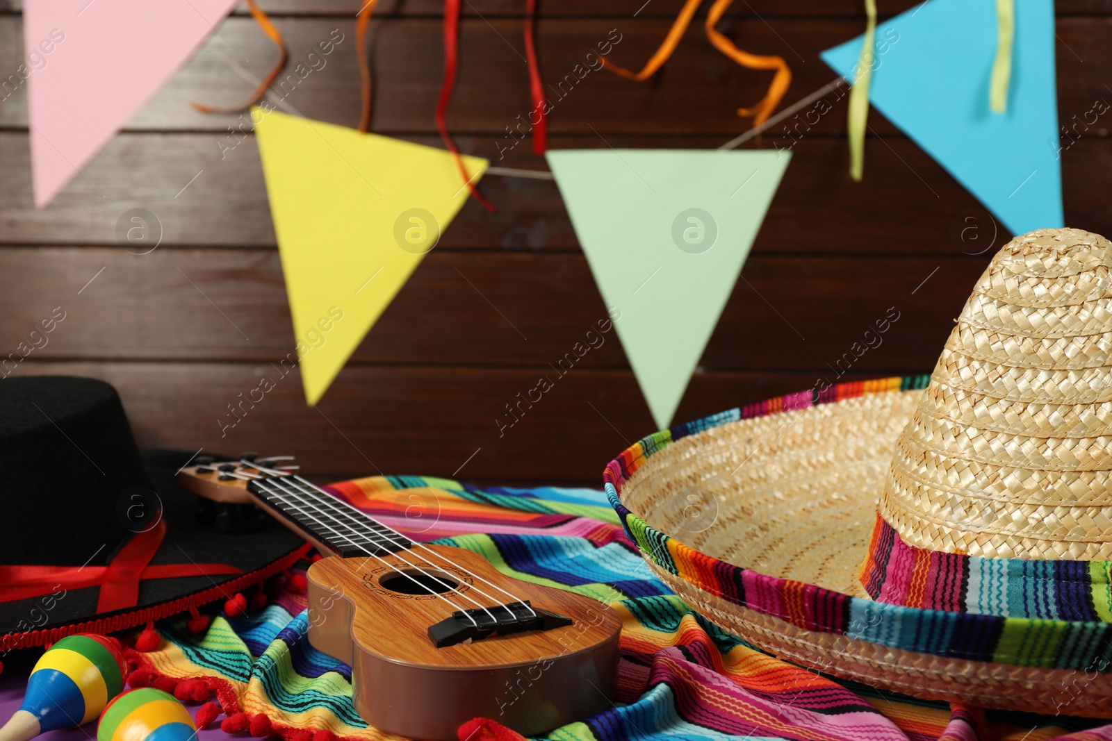 Photo of Mexican sombrero and black Flamenco hats, ukulele and maracas on table, closeup