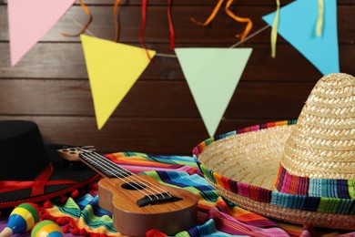 Photo of Mexican sombrero and black Flamenco hats, ukulele and maracas on table, closeup