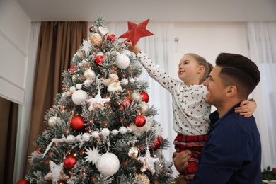 Father and little daughter decorating Christmas tree with star topper indoors