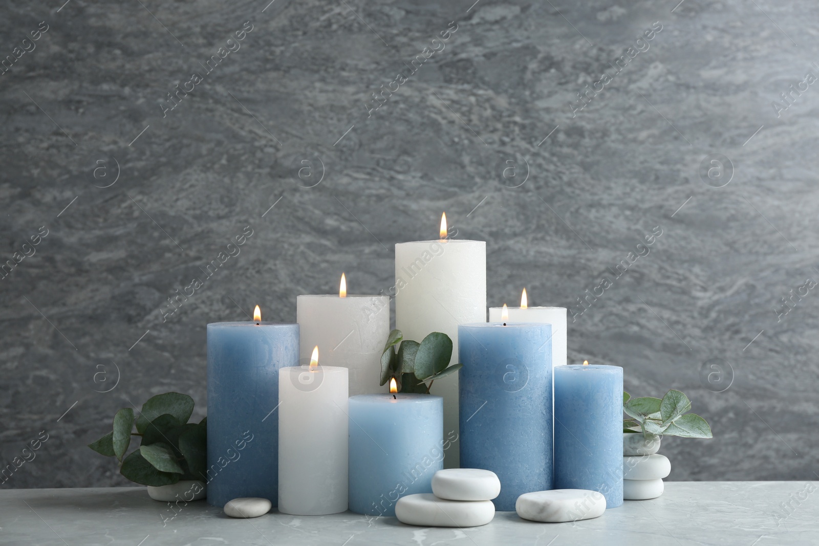 Photo of Set of burning candles with spa stones and eucalyptus on table against grey marble background
