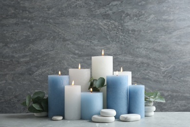 Photo of Set of burning candles with spa stones and eucalyptus on table against grey marble background