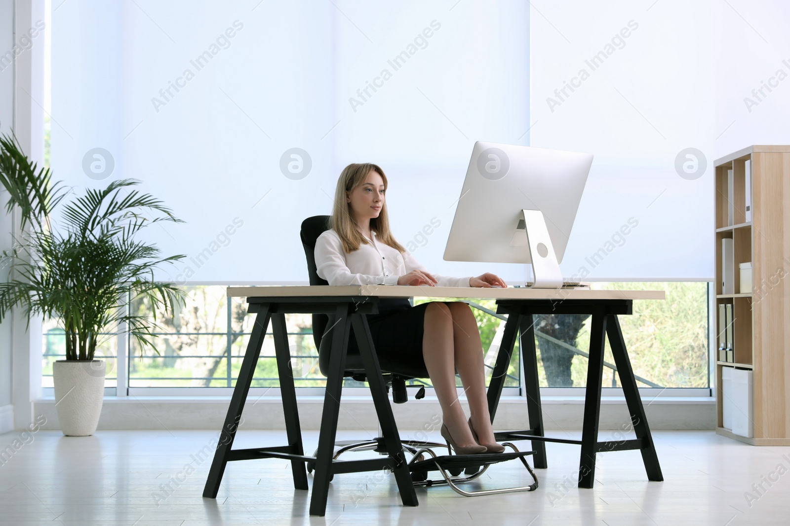 Photo of Woman using footrest while working on computer in office