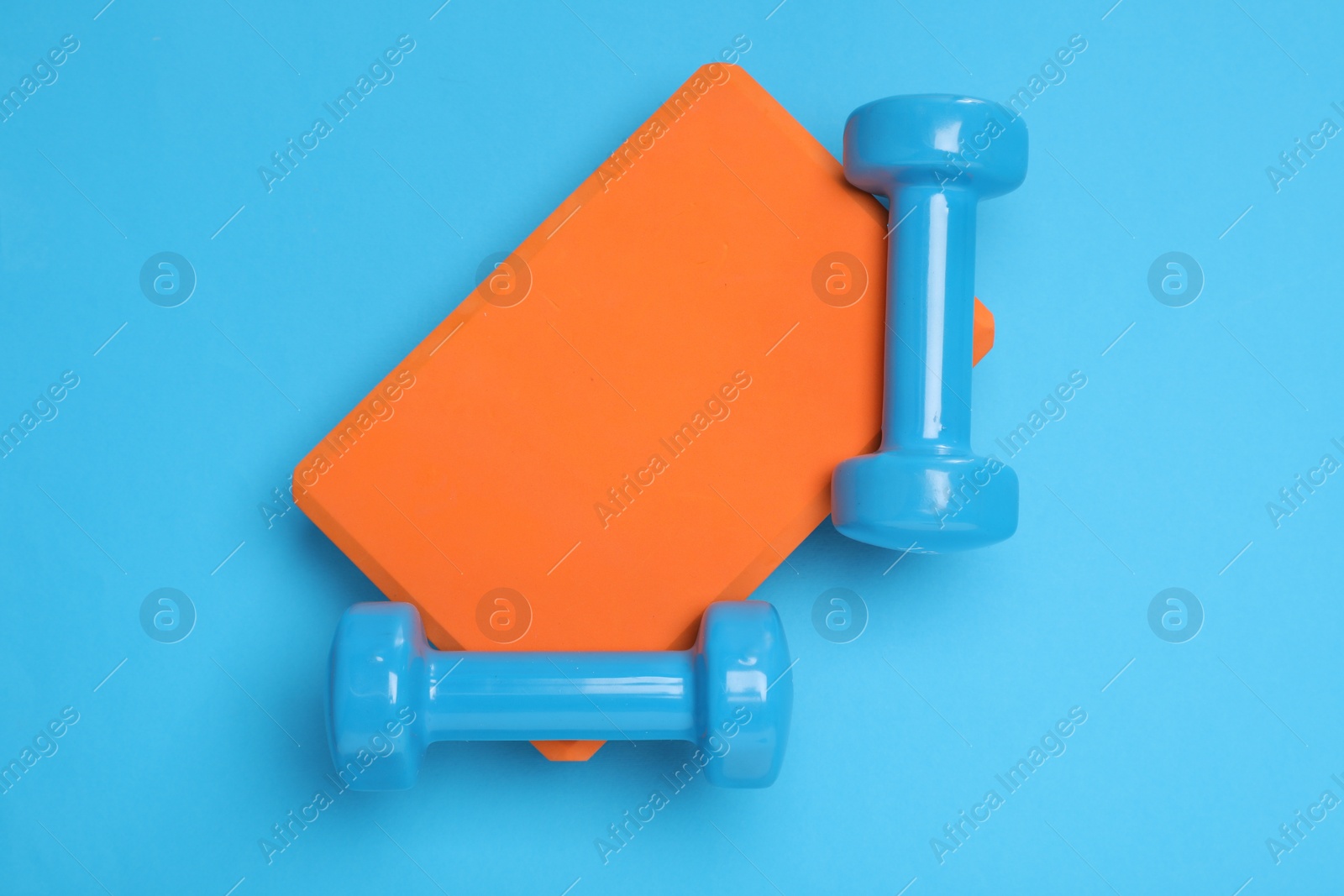 Photo of Two dumbbells and yoga block on light blue background, top view