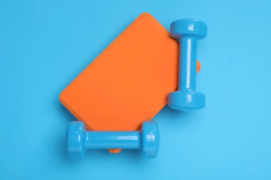 Photo of Two dumbbells and yoga block on light blue background, top view