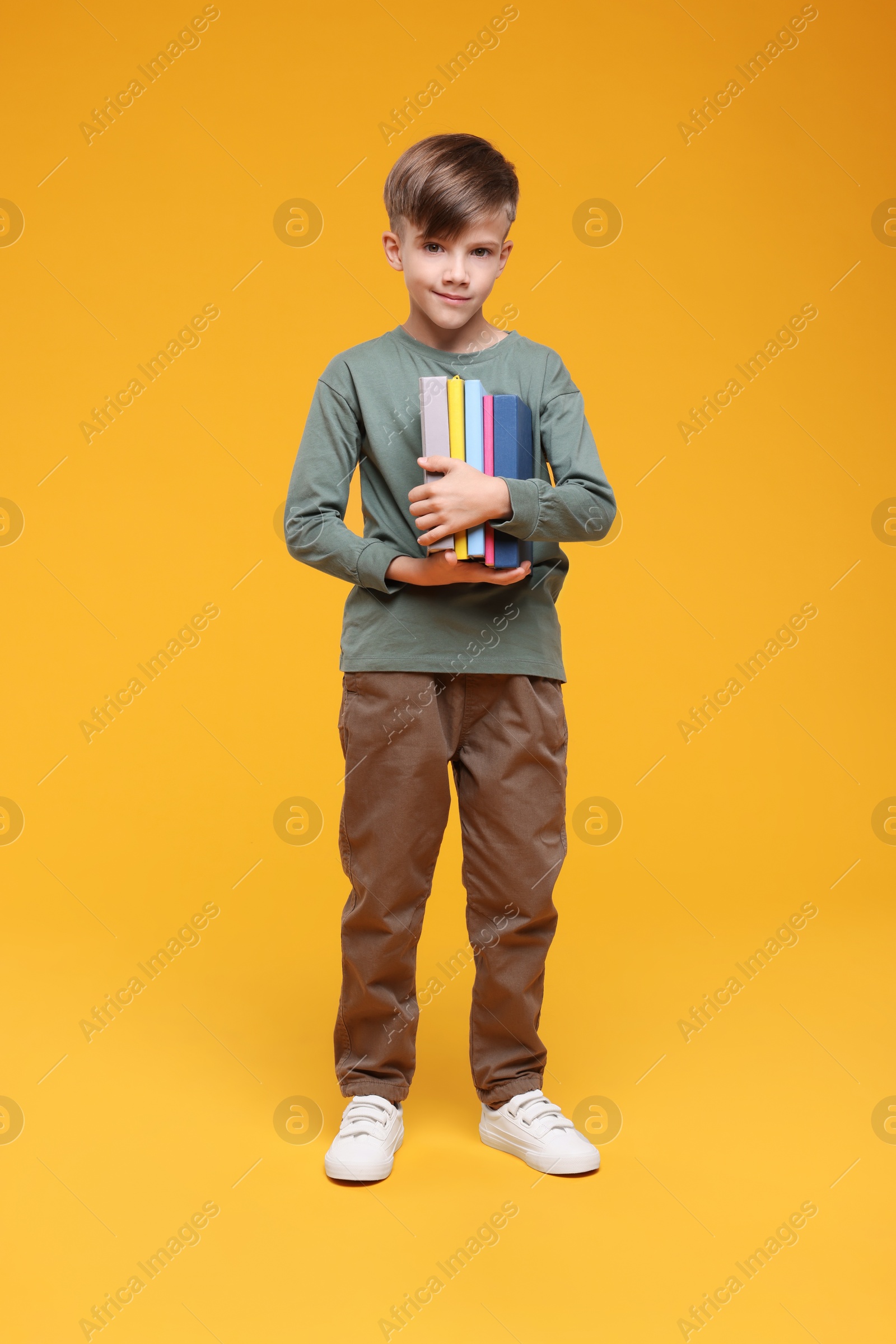 Photo of Cute schoolboy with books on orange background