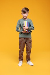 Photo of Cute schoolboy with books on orange background