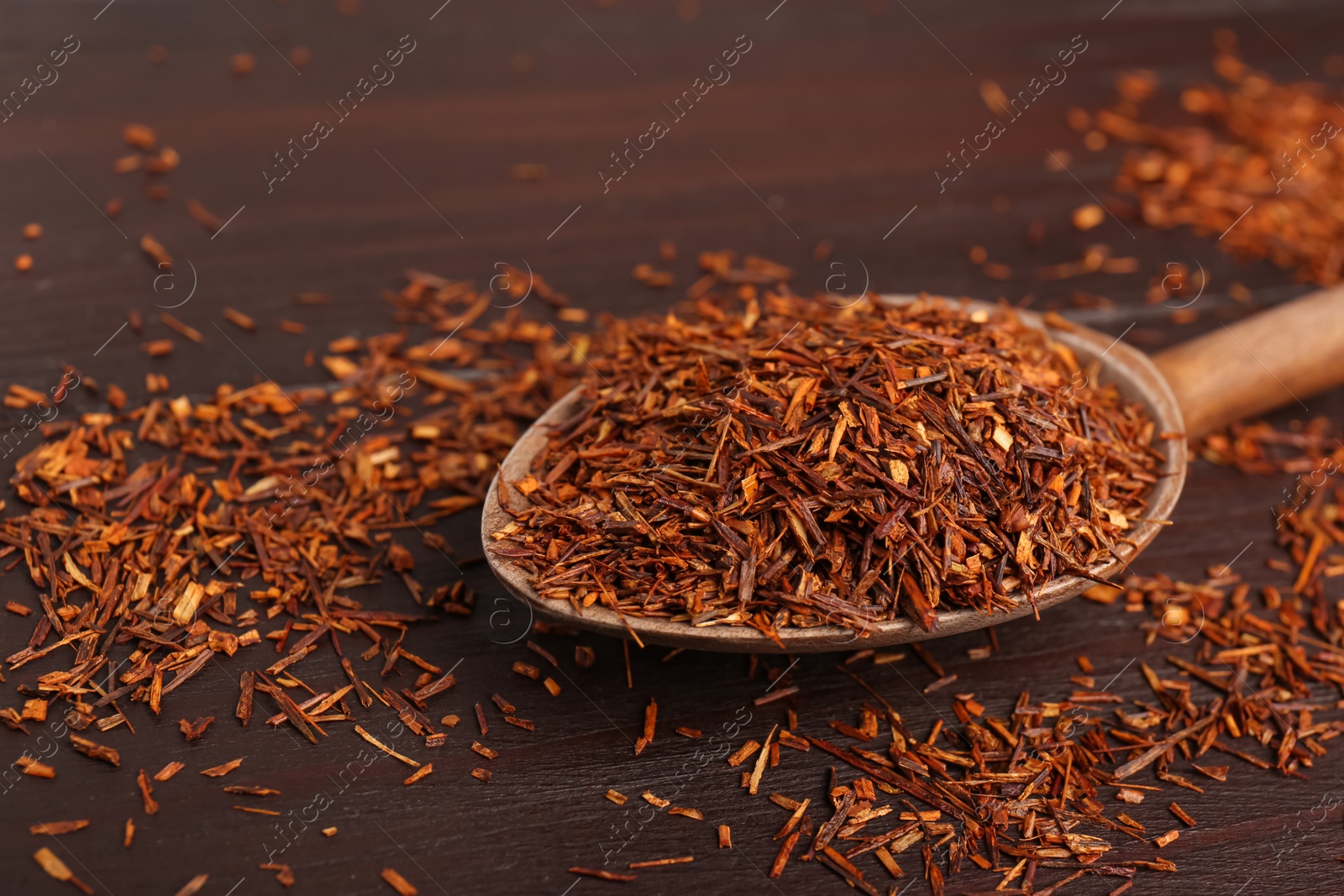 Photo of Spoon with dry rooibos leaves on wooden table, closeup