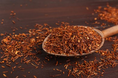 Spoon with dry rooibos leaves on wooden table, closeup