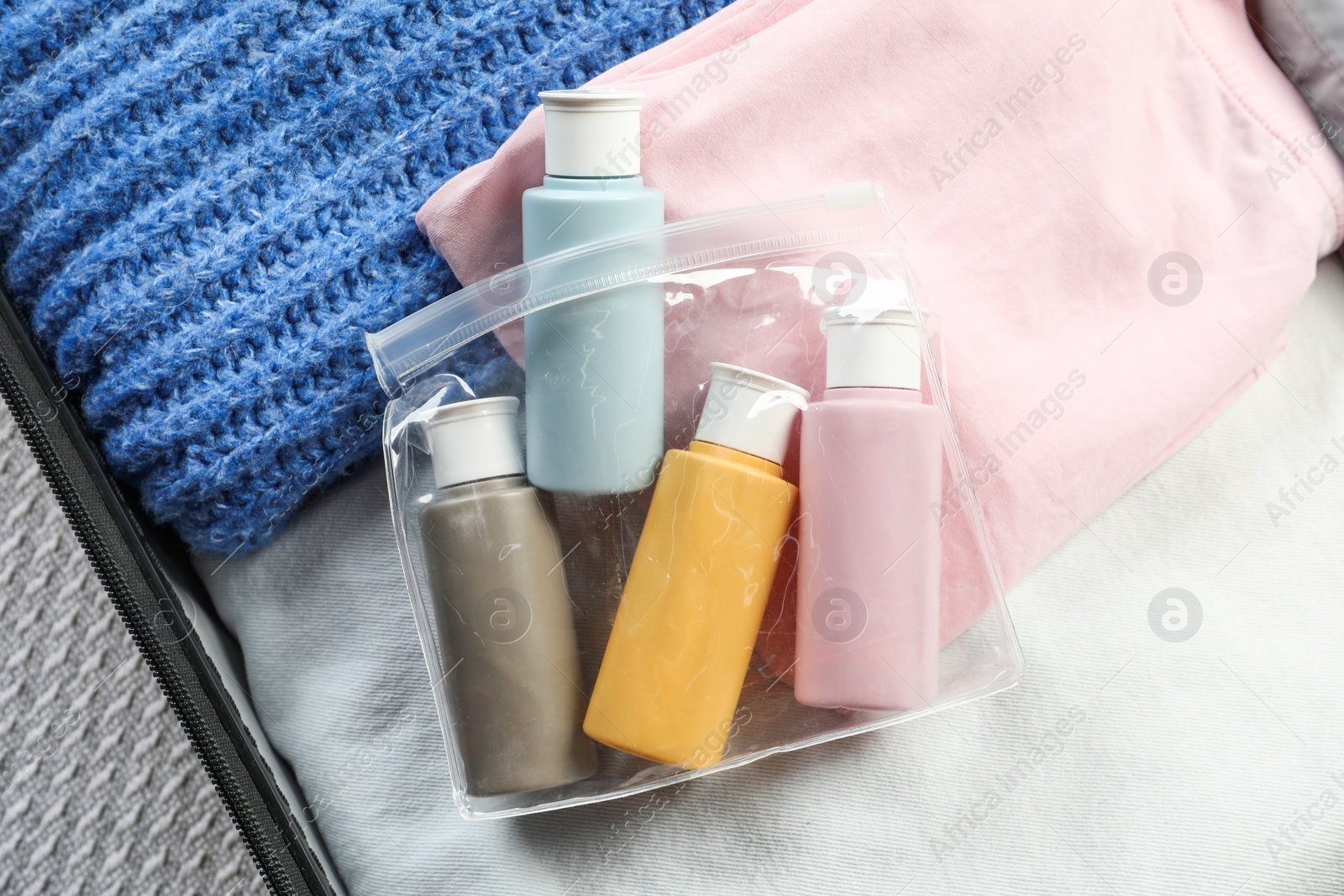 Photo of Plastic bag of cosmetic travel kit in suitcase, top view