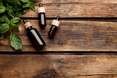 Photo of Bottles of basil essential oil with fresh leaves on wooden table, flat lay. Space for text