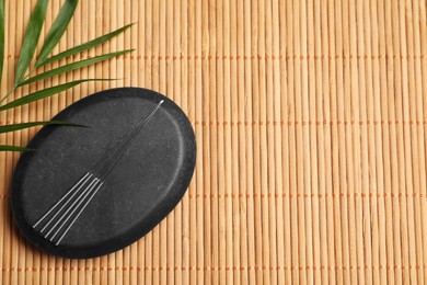 Acupuncture needles, spa stone and leaf on bamboo mat, flat lay. Space for text