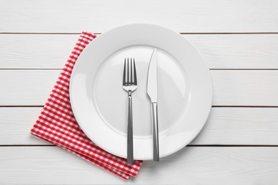 Clean plate with shiny silver cutlery on white wooden table, flat lay