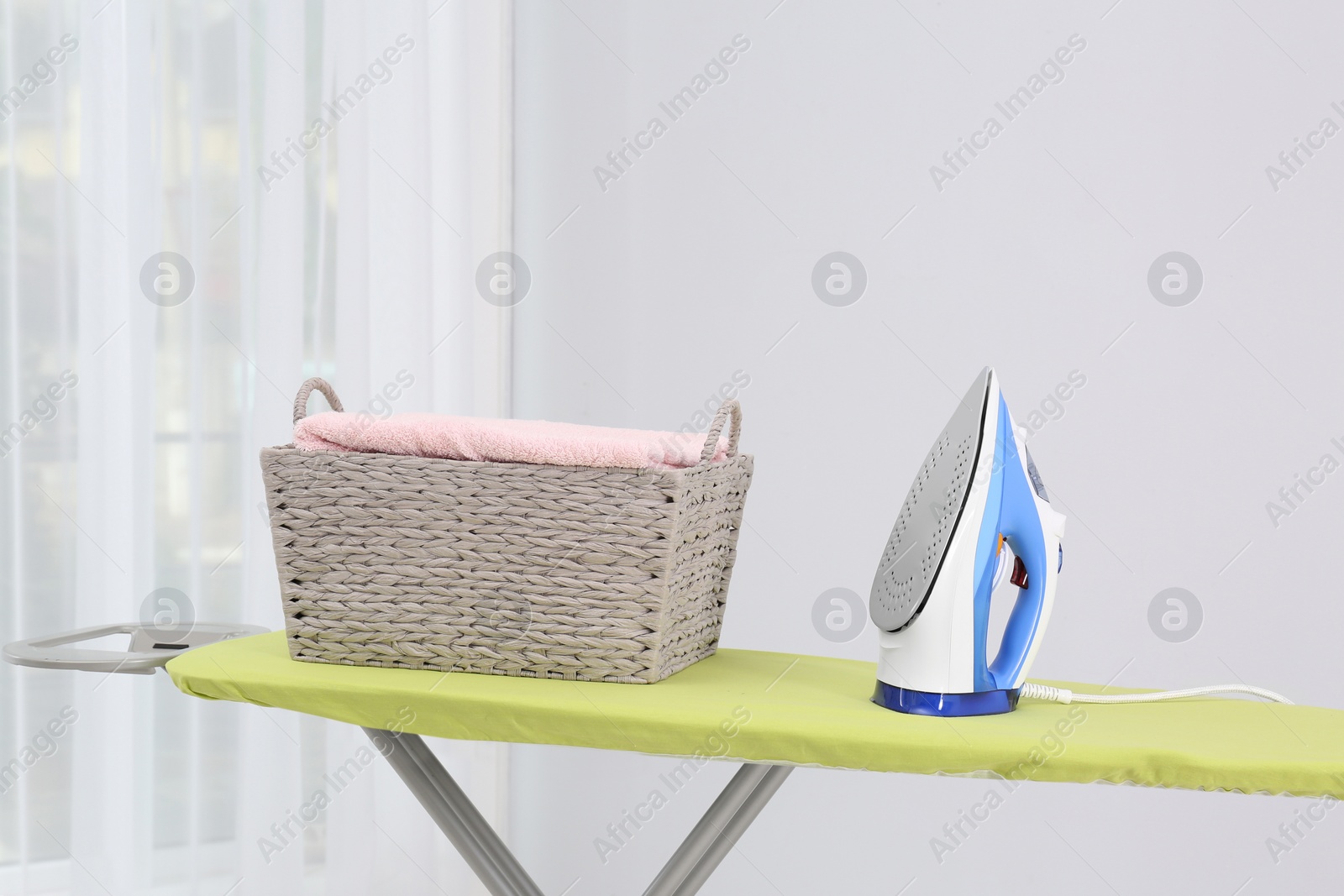 Photo of Board with modern iron and laundry basket in room