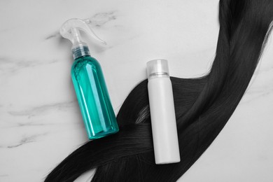 Photo of Spray bottles with thermal protection and lock of brunette hair on white marble table, flat lay